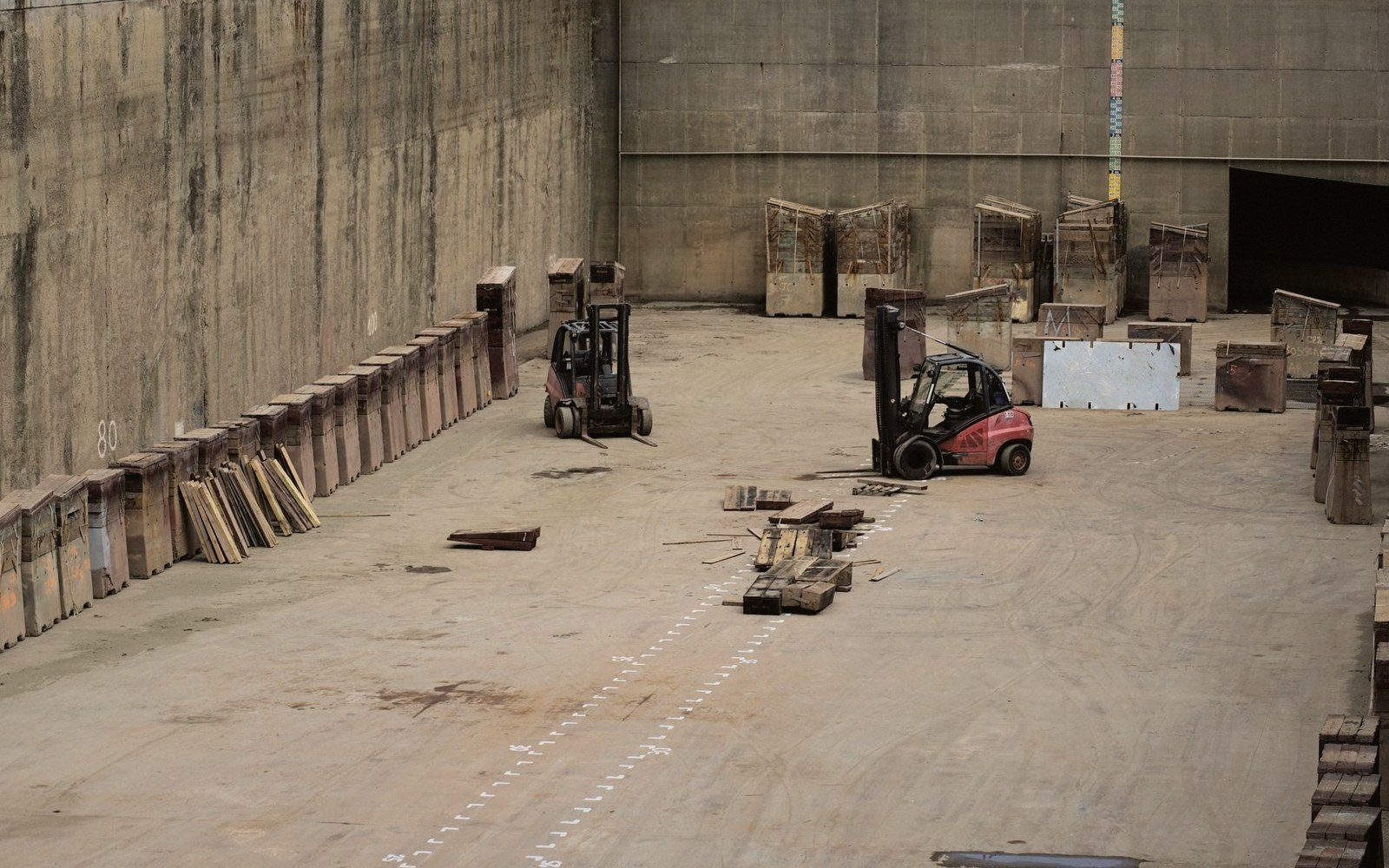Forklifts in a large concrete store, bins along the wall